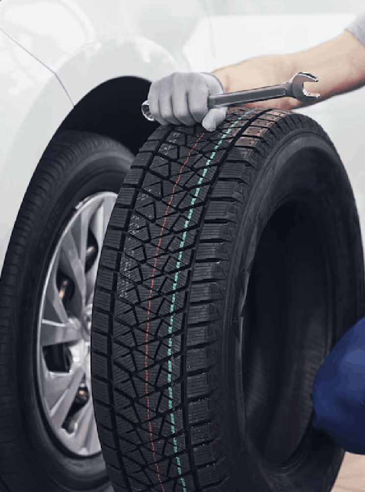 Technician with a blue workwear, holding a wrench and a tire while showing thumb up<br />
