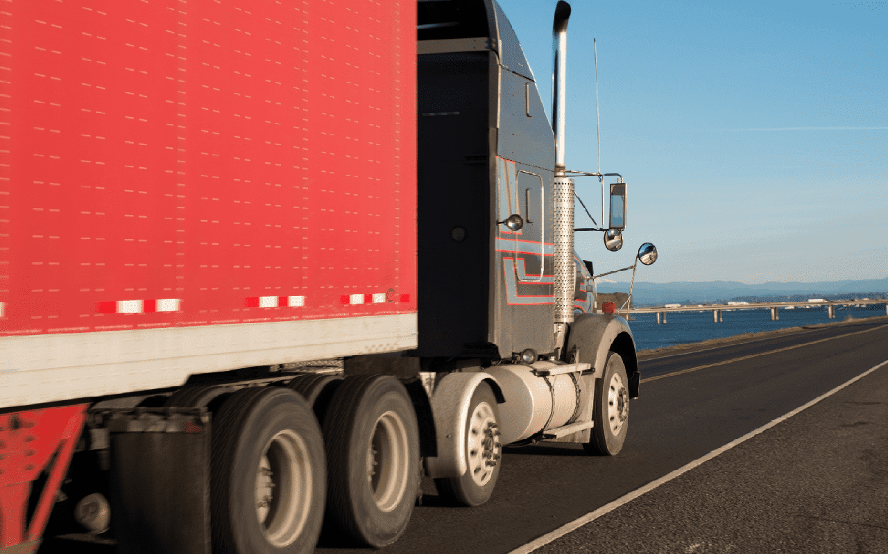 Big dark semi truck and red trailer on the road along the river